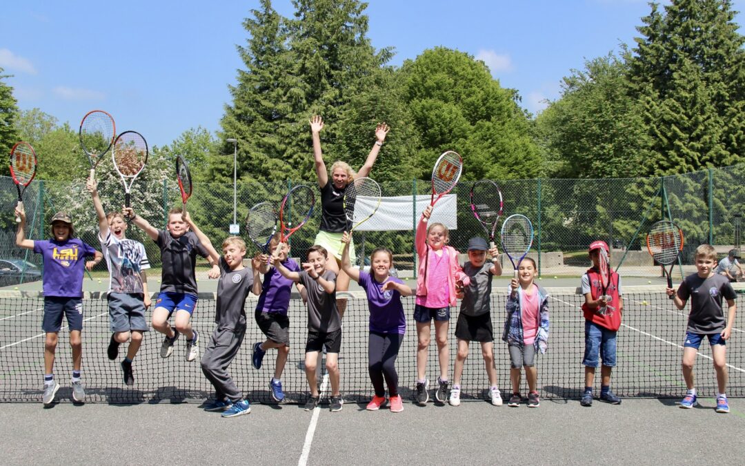 A group of kids working together to improve their tennis skills while holding tennis rackets.