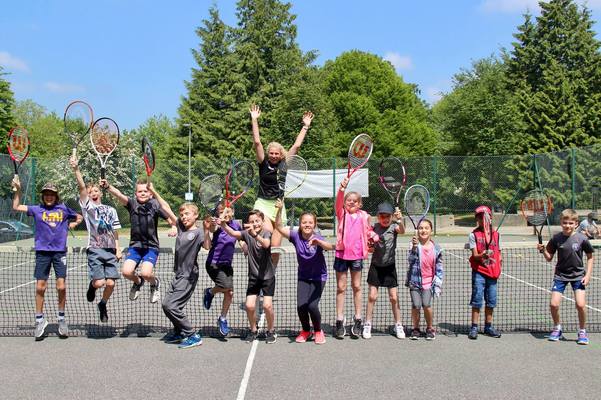 A group of children from the Kings Hill Community posing with tennis rackets on a tennis court at the Tennis Club.